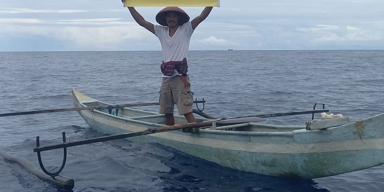 Seorang aktivis Jala Ina membentangkan poster penolakan PP Penangkapan Ikan Terukur di WPP-NRI 714 Perairan Laut Banda, Kamis, 6 April 2023. (Foto: Jala Ina)